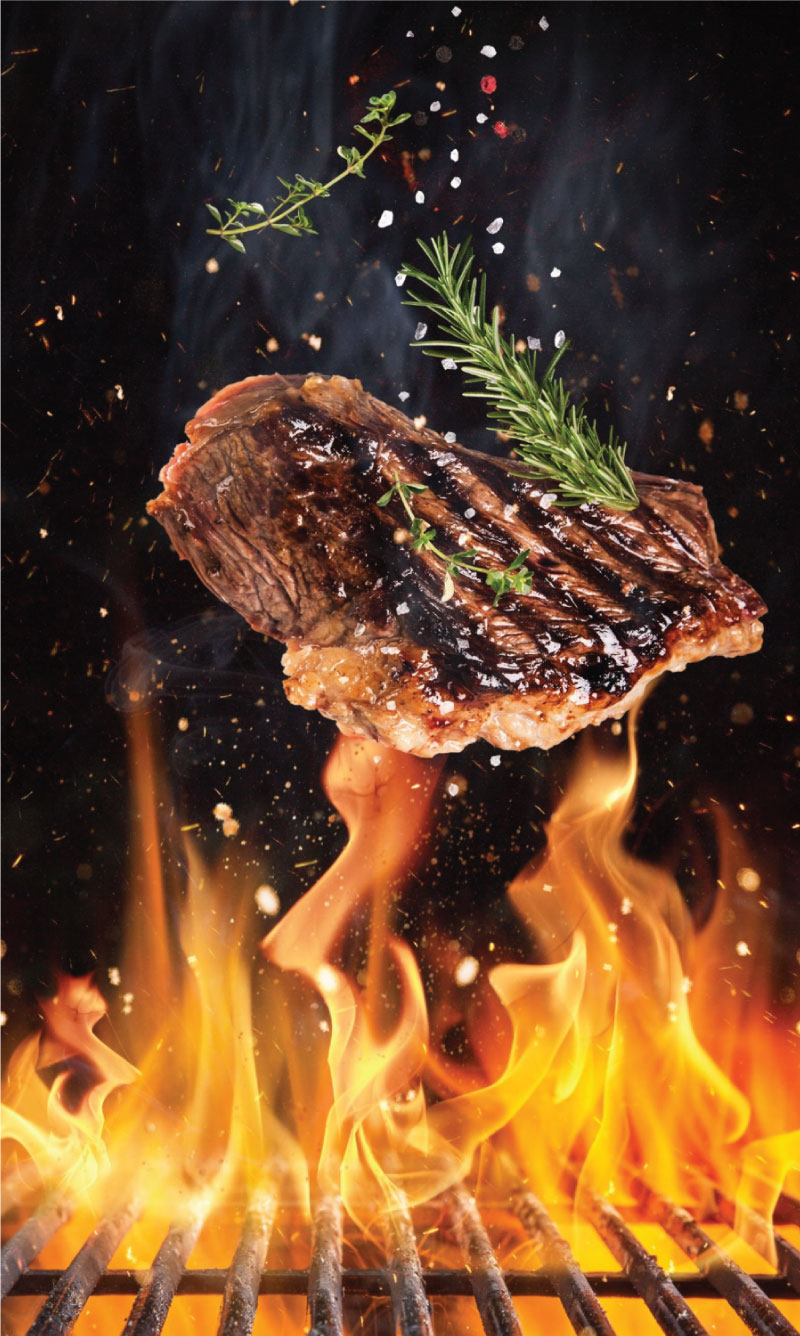 Tasty beef steaks flying above cast iron grate with fire flames